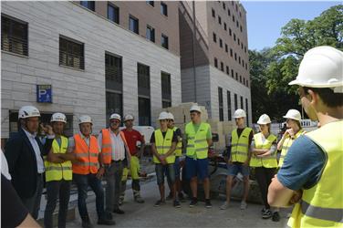 Amtsdirektor Andrea Sega, Lehrer Harald Seppi, Baustellenleiter Michael Egger, Bauleiter Enrico Guglielmon und Vorarbeiter Florian Prast mit den Schülern auf der Baustelle am Magnago-Platz (FOTO: LPA/Lidia Canins)