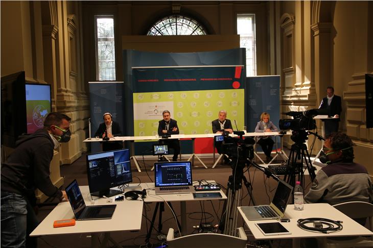 Virtuelle Medienkonferenz vom 31. März mit (v.l.) Achammer, Kompatscher, Schuler und Deeg. Rechts LPA-Chefredakteur Guido Steinegger, im Vordergrund die Kameraleute von Gnews (Foto LPA/Fabio Brucculeri)