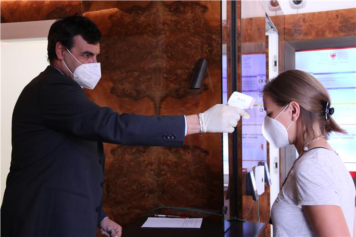 Mitarbeiter in Landhaus 1 in Bozen machen es vor: Messen der Körpertemperatur mit Lasergerät und - zwecks größtmöglichen Abstands - mit gestrecktem Arm (Foto: LPA/Fabio Brucculeri)